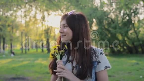 美丽的年轻女子微笑着闻着公园里的鲜花视频的预览图