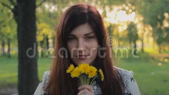 美丽的年轻女子微笑着闻着公园里的鲜花视频的预览图