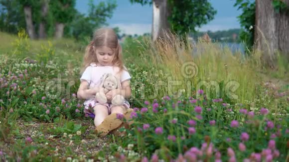 一个小女孩和一只玩具兔子在草地上的四叶草中玩耍视频的预览图