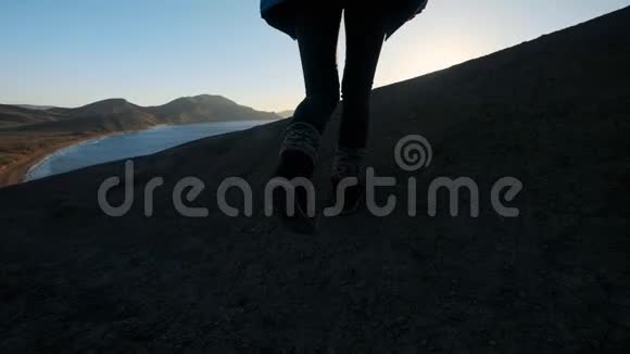 年轻迷人的女孩徒步旅行者沿着沙质悬崖或海边悬崖举起双手看着金色视频的预览图