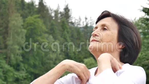 一位年长的女士在森林和山脉的外面为上臂做伸展运动视频的预览图