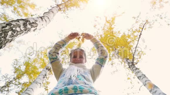 快乐的女人在秋天公园穿针织毛衣快乐而兴奋的年轻女子在玩着把黄叶扔进去视频的预览图