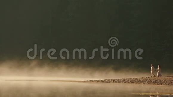 幸福的乡下夫妇穿着乌克兰民族的衣服在夕阳的金色薄雾中漫步在岩石海岸上视频的预览图