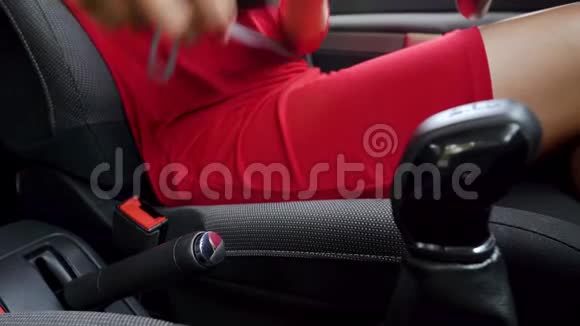 在驾驶前身着红色礼服的女士在车内系紧安全带视频的预览图