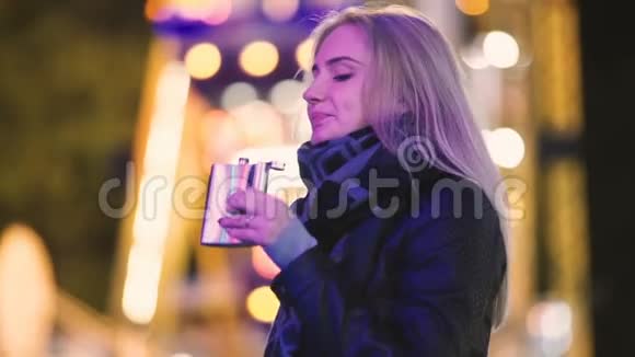 年轻漂亮的女人独自从烧瓶里喝威士忌酒晚上在游乐园的户外活动夜城背景视频的预览图