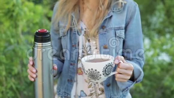 留着长发的在模糊的自然背景下手里拿着一杯茶或咖啡是个漂亮女人视频的预览图