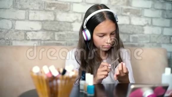 可爱的女孩戴着耳机和家庭服装听音乐用文件做指甲抛光指甲视频的预览图