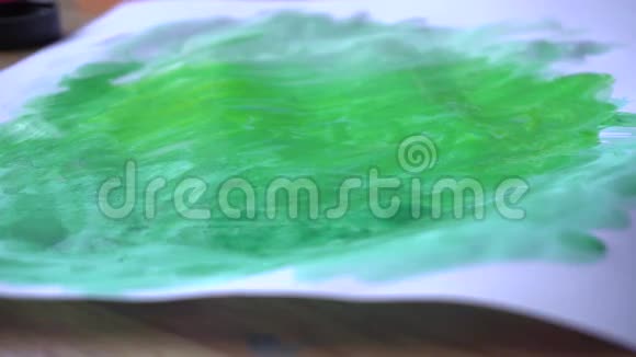 一个女孩用画笔和绿色颜料在一张纸上作画视频的预览图