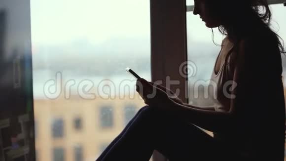 一个身材矮小的女人拿着一杯咖啡坐在窗台上用手机1920x1080视频的预览图