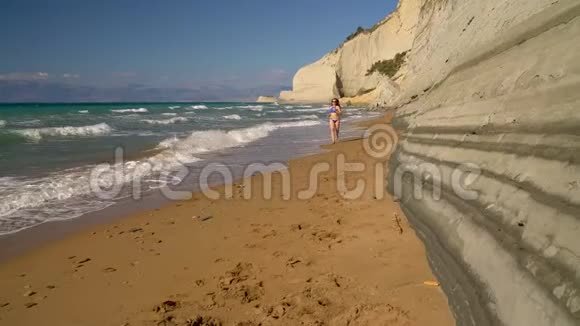 海滩比基尼女郎无忧无虑地沿着海滩上的水奔跑希腊科孚海岸风景如画视频的预览图