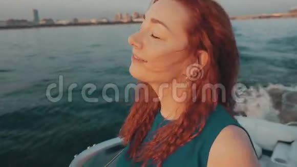 红发女孩穿着绿松石的衣服在摩托艇上航行美丽的日落放松放松视频的预览图