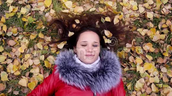 美丽幸福的年轻女子戴着耳机躺在秋叶上听音乐季节科技和人视频的预览图