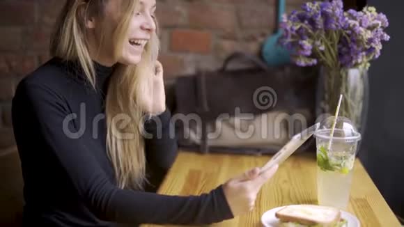 快乐可爱的大学生使用平板电脑他坐在咖啡馆里手里拿着一块平板电脑看着视频的预览图