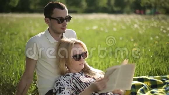 在日落时分爱一对戴着太阳镜的情侣在田野上用蒲公英读书视频的预览图