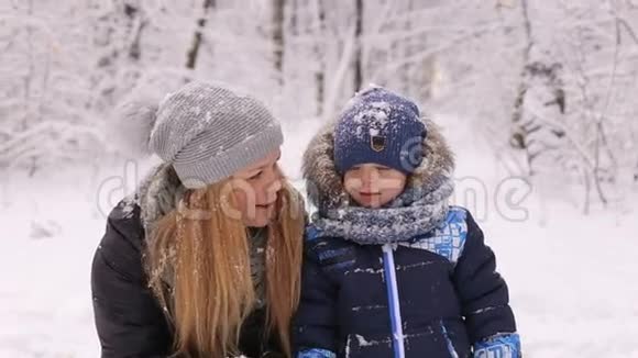 一位年轻的母亲和她的儿子在冬天的森林里玩雪视频的预览图