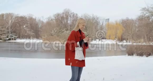 穿着红色冬衣的年轻女孩在城市公园里用手机视频的预览图