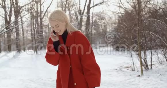 穿着红色冬衣的年轻女孩在城市公园里用手机视频的预览图