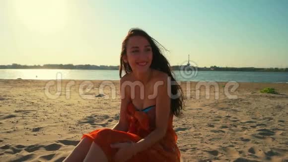 自由快乐的女人享受日落美丽的女人坐在沙滩上金色的阳光下夕阳西下看着相机视频的预览图