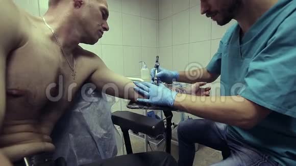 纹身艺术家在工作男人画在他手臂上的女人的脸上快关门纹身沙龙视频的预览图