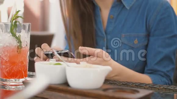 布鲁内特女孩使用智能手机而坐在外面的咖啡馆喝一杯清凉的饮料从吸管4k视频的预览图