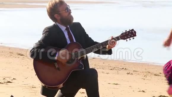 吉他手停止演奏把手伸向沙滩上的金发女孩视频的预览图