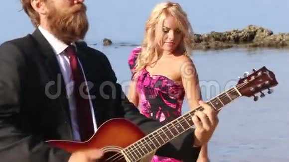 穿着蝴蝶结裙子的女孩在海滩上由吉他手跳舞视频的预览图