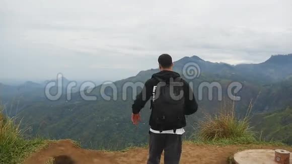 年轻的男性徒步旅行者背包伸向山顶举起双手站在边缘的观光客视频的预览图
