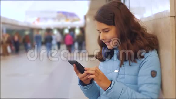 十几岁的女孩带着智能手机和耳机等待地铁很多人挤在地下交叉路口地铁地下视频的预览图