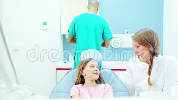 友好的牙医与年轻病人交谈而助手则检查她视频的预览图
