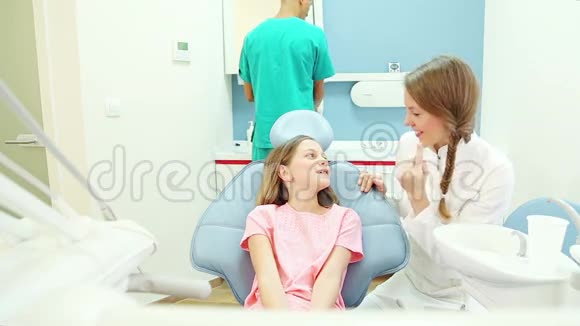 友好的牙医与年轻病人交谈而助手则检查她视频的预览图