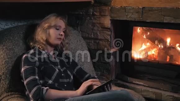 使用数码平板电脑坐在壁炉旁的年轻女子视频的预览图