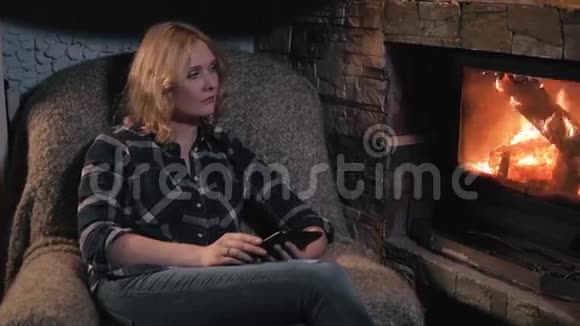 使用数码平板电脑坐在壁炉旁的年轻女子视频的预览图