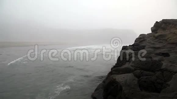 笼罩在雾中的大岩石周围温和的海浪视频的预览图