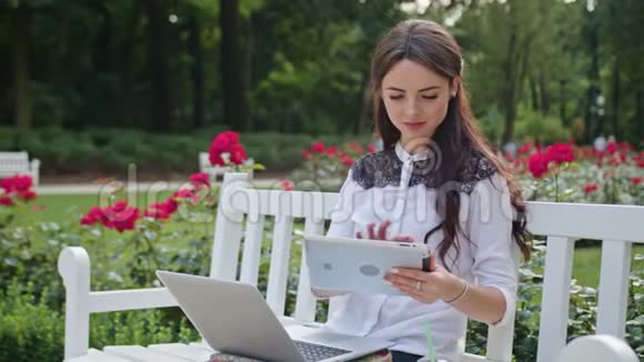 公园里的女士用笔记本电脑和平板电脑视频的预览图
