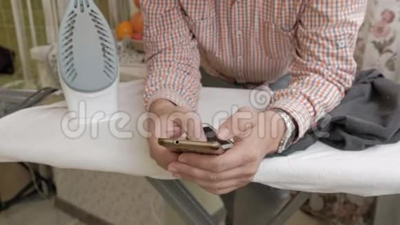 一个男人在他家的熨衣板上抚摸他的衬衫用智能手机视频的预览图