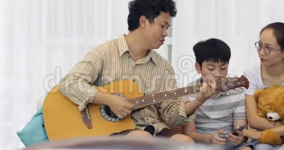 快乐的亚洲父亲在家为家人弹吉他视频的预览图