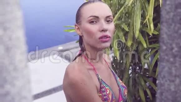 一位身穿比基尼的金发女人在游泳池里沐浴周围是热带花园视频的预览图