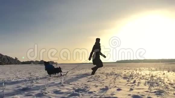 坐雪橇的小男孩妈妈哄着他可爱的孩子家庭冬季户外活动幸福的家庭视频的预览图