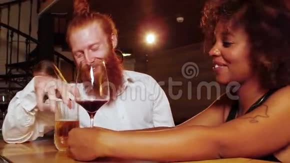 一个留着姜胡子的嬉皮士和一个非常漂亮开朗的黑人女人在豪华酒吧里调情他们聊天喝饮料视频的预览图