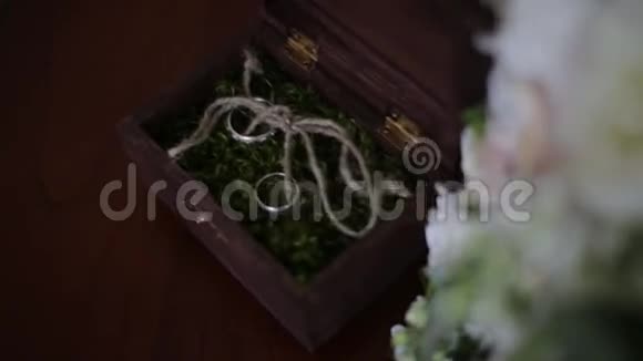 婚礼戒指放在一个装满苔藓的木箱里婚礼戒指的木箱靠近新娘花束视频的预览图