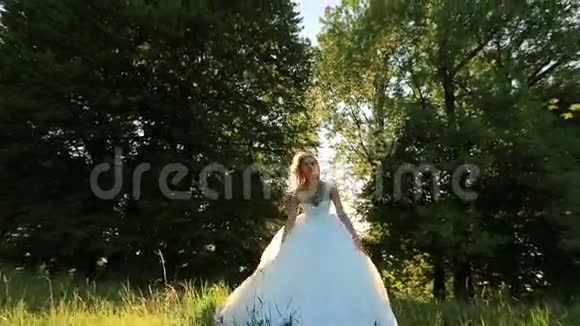 迷人的年轻金发新娘在阳光明媚的夏日在绿色草地上跳跃和玩耍视频的预览图