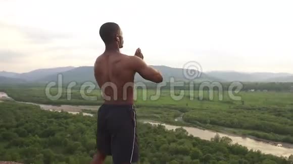 肌肉发达的非裔美国健美运动员祈祷的双手伸展在山顶在他的早晨户外视频的预览图