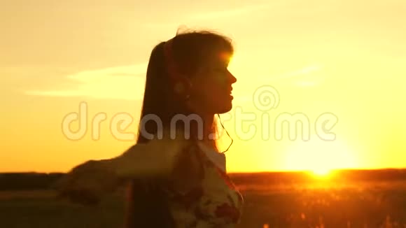 美丽的女孩戴着耳机和智能手机在温暖的夕阳下飞行快乐的女孩视频的预览图