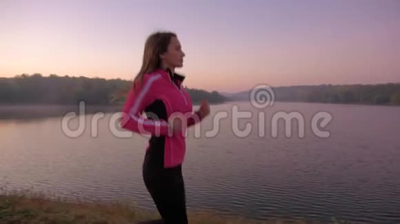 日出时在湖边奔跑的年轻女子视频的预览图