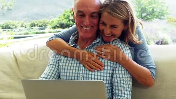 微笑的高级女性拥抱一个男人同时使用笔记本电脑视频的预览图
