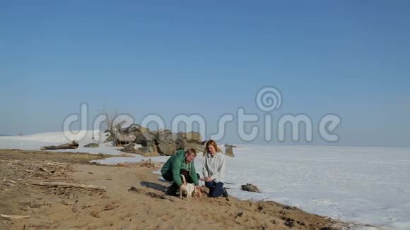 一对夫妇带着一只狗沿着冰冻的湖岸散步视频的预览图