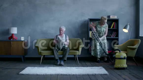 一位老年妇女正在打扫地板一位老年男子正在看报纸和电视视频的预览图