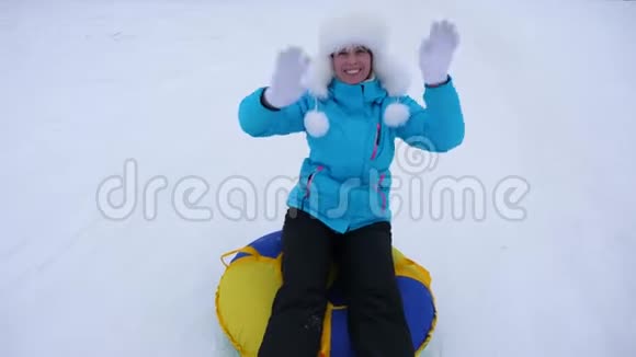 美丽的年轻女子在雪地里滑过充气的雪管和波浪手快乐的女孩滑过雪地视频的预览图