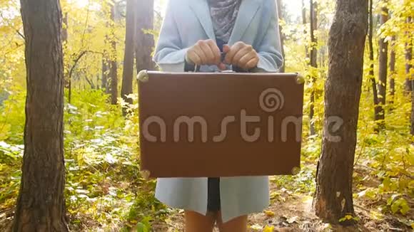一位在秋天公园里提着手提箱的年轻女子视频的预览图