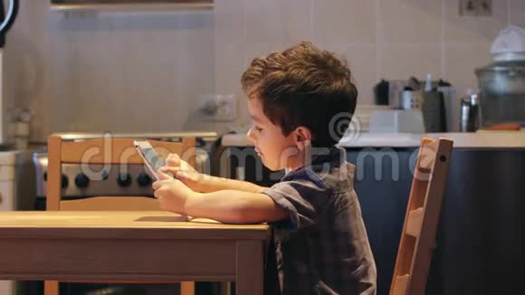侧视图一个可爱的小孩在家里的桌子上使用平板电脑休闲服装视频的预览图